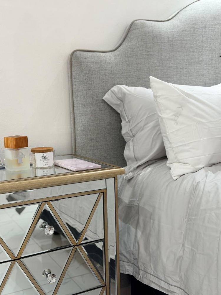 A bedroom with a tall upholstered headboard and wall lights
